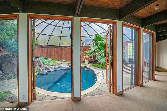 The pool is surrounded by large windows and glass doors and surrounded by tropical flora