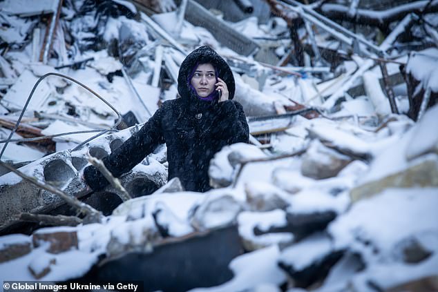 A woman speaks on the phone while standing amid the rubble of a high-rise residential building on January 3, 2024 in Kiev