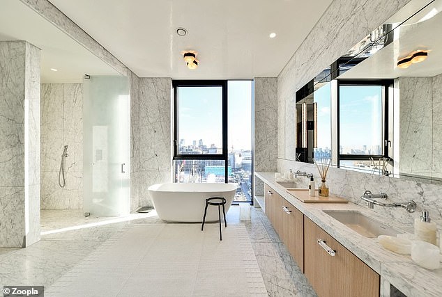 This penthouse bathroom features a bathtub with skyline views and floor-to-ceiling marble