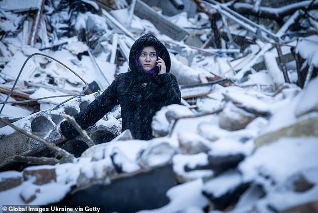 A woman speaks on the phone while standing amid the rubble of a high-rise residential building on January 3, 2024 in Kiev