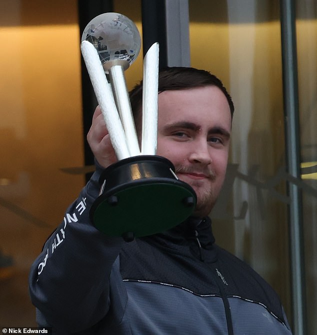 Littler shows off his second trophy of the PDC World Darts Championship as he leaves his hotel on Thursday morning