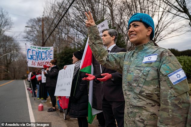 A woman dressed in an Israeli uniform holds a peace sign as a man resembling Blinken extends his hands covered in blood