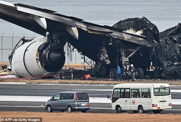 Officials look at the burned wreckage of a Japan Airlines (JAL) passenger plane on the tarmac of Tokyo International Airport in Haneda in Tokyo