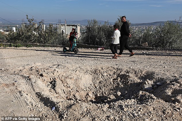 People walk past a crater left by an explosive device that killed an Israeli officer during an Israeli raid on Jenin in the occupied West Bank