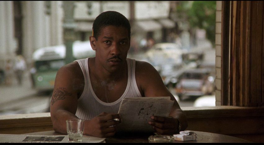 Denzel Washington, wearing a white tank top, reads the newspaper in Devil in a Blue Dress.
