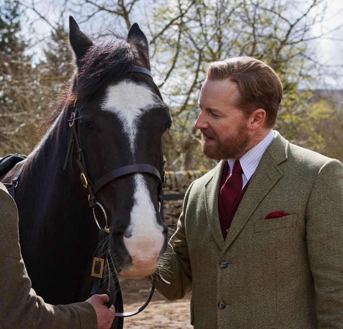 Siegfried wears a wool suit and looks admiringly at a horse in All Creatures Great and Small.