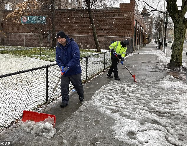 Workers clear snow and slush from the sidewalk in Cambridge, Massachusetts, on Sunday