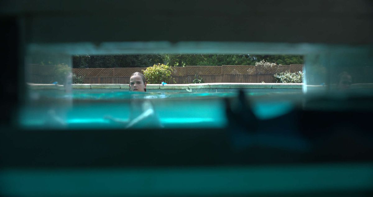 A child watches a pool skimmer, which we see from the skimmer's perspective in Night Swim