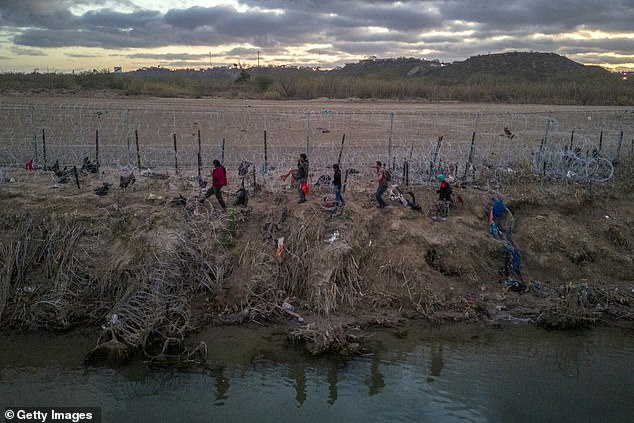 Migrants walk past razor wire over which President Biden and Governor Greg Abbott argue after crossing the Rio Grande