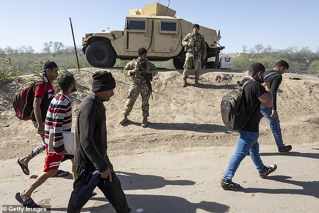 Migrants pass Texas National Guard soldiers guarding the U.S. border