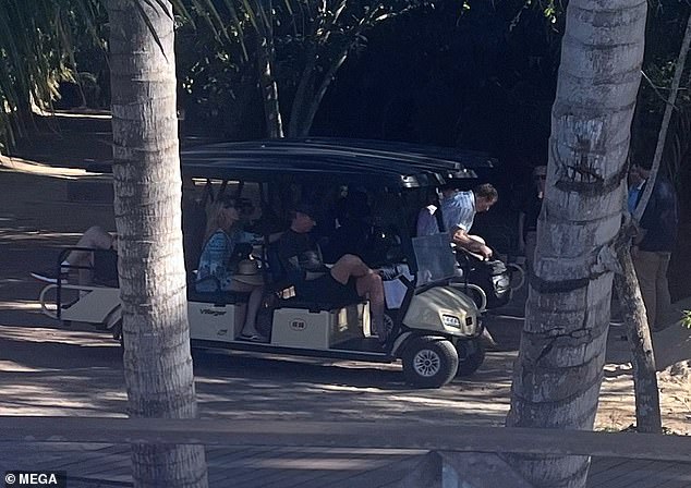 Gavin Newsom, wearing a black baseball cap and black shorts, sits in front of his wife