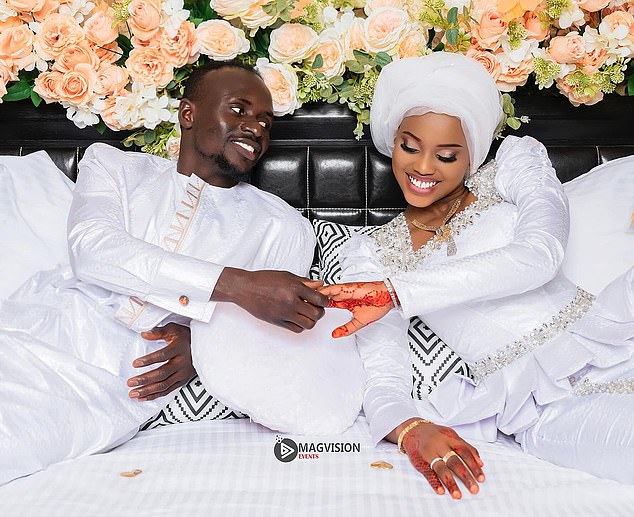 The couple holds hands and smiles with a floral background behind them