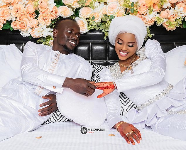 The couple holds hands and smiles with a floral background behind them