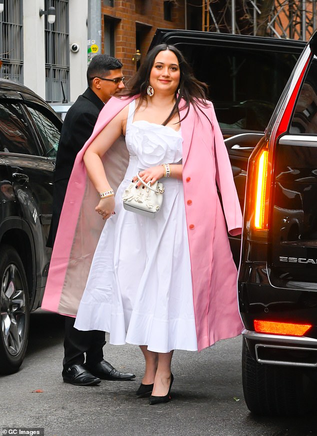 Her second outfit was built around a luminous white dress that reached just above her ankles with a voluminous skirt.  The look, with thick straps, featured a beautiful floral fabric design that covered her bust.  She added some color with her pale pink overcoat