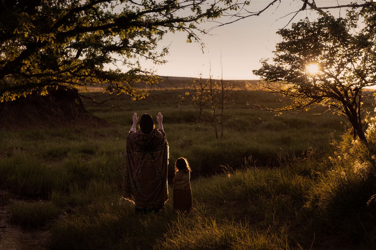 A beautiful shot at sunset of Mollie (Lily Gladstone) praying to the sun with her daughter in a field