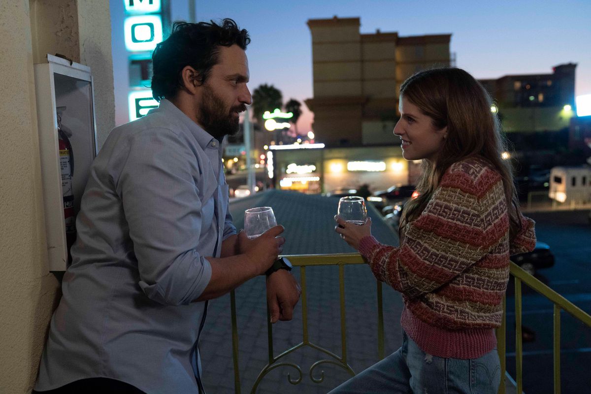 (L-R) Jake Johnson and Anna Kendrick stand on a balcony drinking from stemless glasses in Self Reliance.