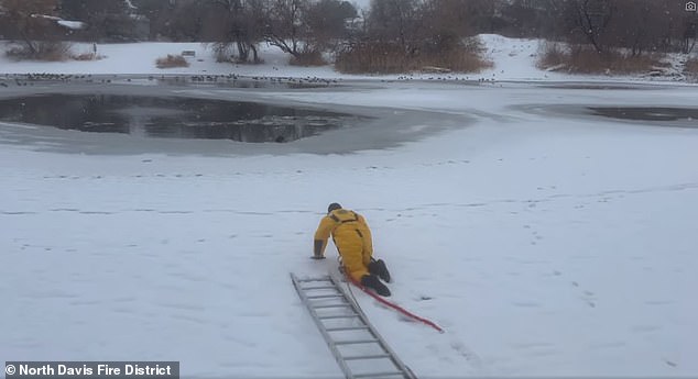 Hadley is seen crawling toward the icy pond wearing a bright yellow dry suit, black ski mask and black boots.  He is attached to a rope harness that his crew members were holding on to