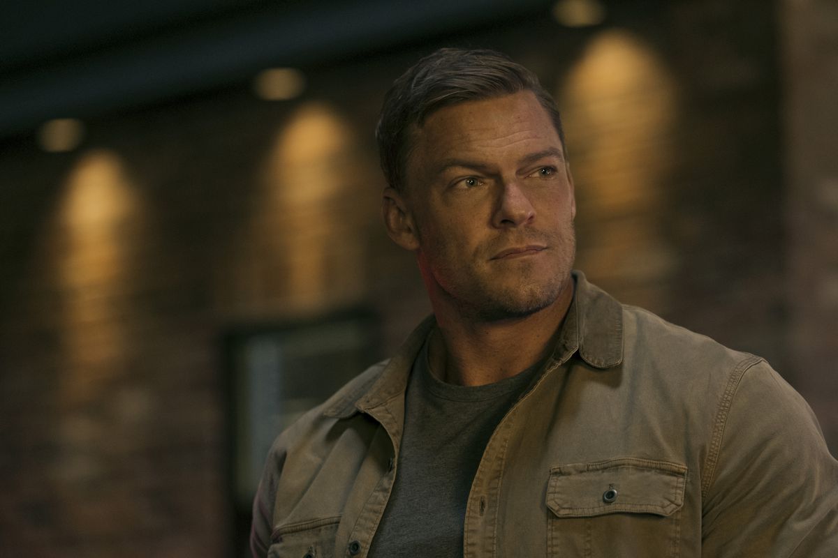 A close-up of Jack Reacher, a very large man, wearing a jacket and looking into the distance, probably at someone smaller than him