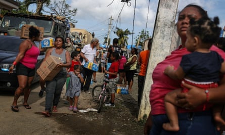 A sort of chaotic angle shot of mostly women and children surrounding an army truck, with a man in camo standing on top with a machine gun in his hand.