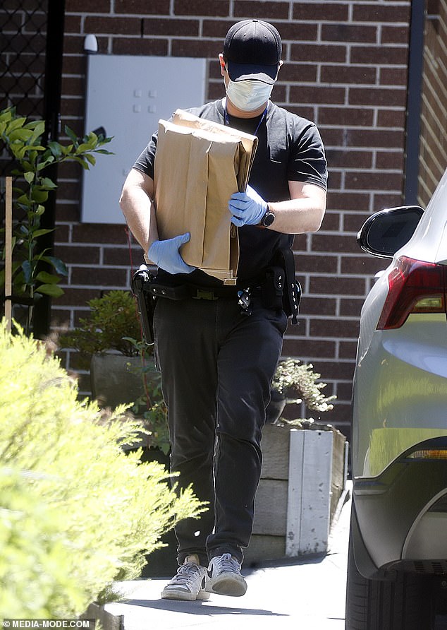 A detective carries two cardboard evidence bags out of the house