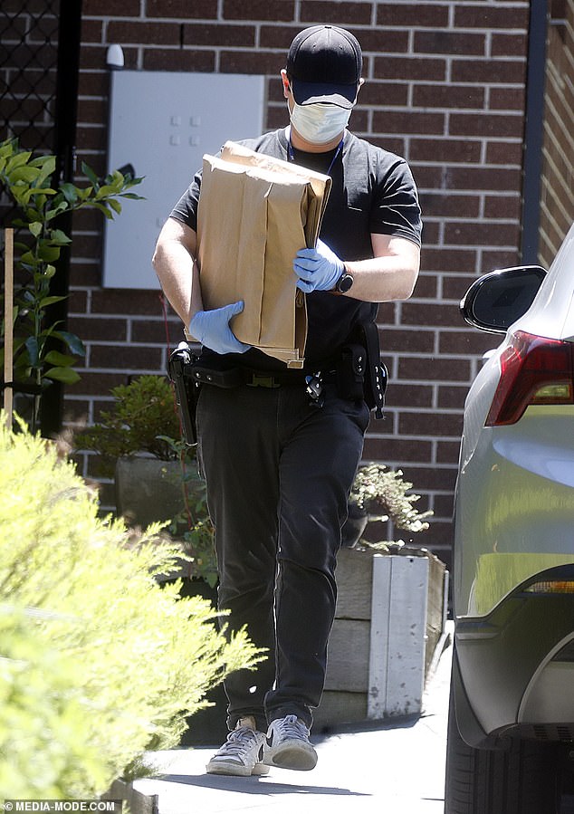 A detective carries two cardboard evidence bags out of the house