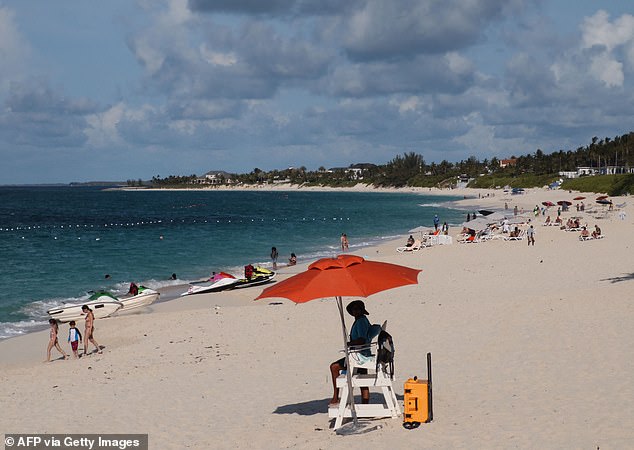 A lifeguard sits under the beach umbrella while watching people enjoy Paradise Island beach, Nassau, Bahamas