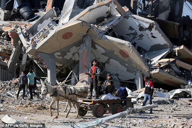 A donkey cart drives past a collapsed building in the Al-Maghazi refugee camp in central Gaza Strip on January 16, 2024