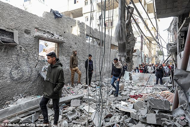 Palestinians, whose buildings were damaged since they were near the targeted Al-Hut family building, are seen standing around the rubble of the buildings as Israeli attacks continue in Gaza's Rafah on Wednesday.