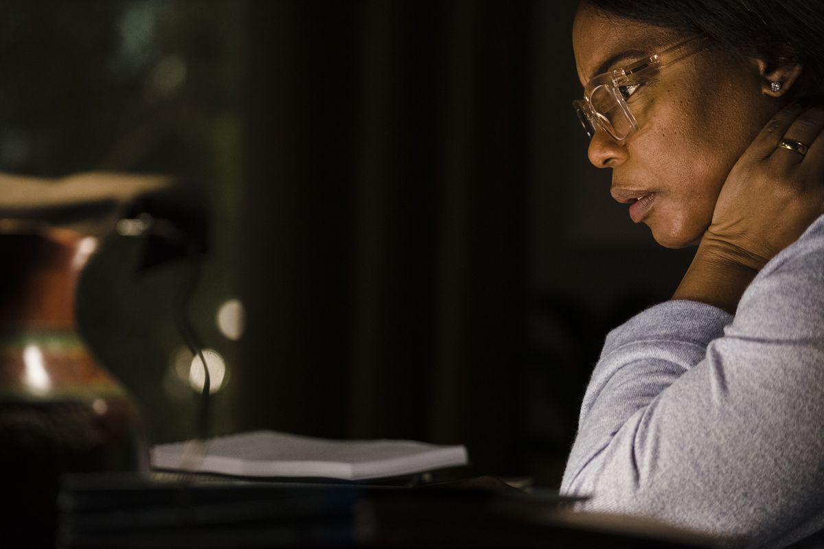 Aunjanue Ellis-Taylor, wearing glasses and dimly lit at night in a close-up, in Origin