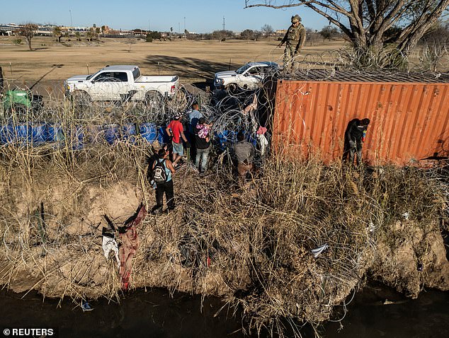 A U.S. National Guard soldier stands on a shipping container as a group of migrants attempt to pass through a concertina wire fence on the banks of the Rio Grande River in Eagle Pass, Texas, U.S., January 17