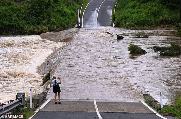 A woman is seen taking a photo of the Coomera River flooding Clagiraba Road on the Gold Coast on January 2