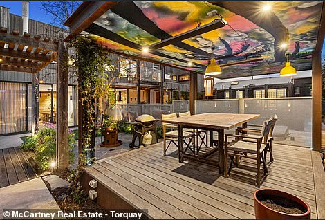 A fire pit borders a small pavilion beneath a colorfully painted covered outdoor area, while a playground features an in-ground trampoline and a number of uneven bars