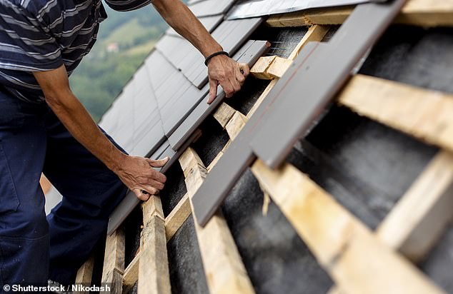 A trader is shown laying black slates on the roof of a new construction project