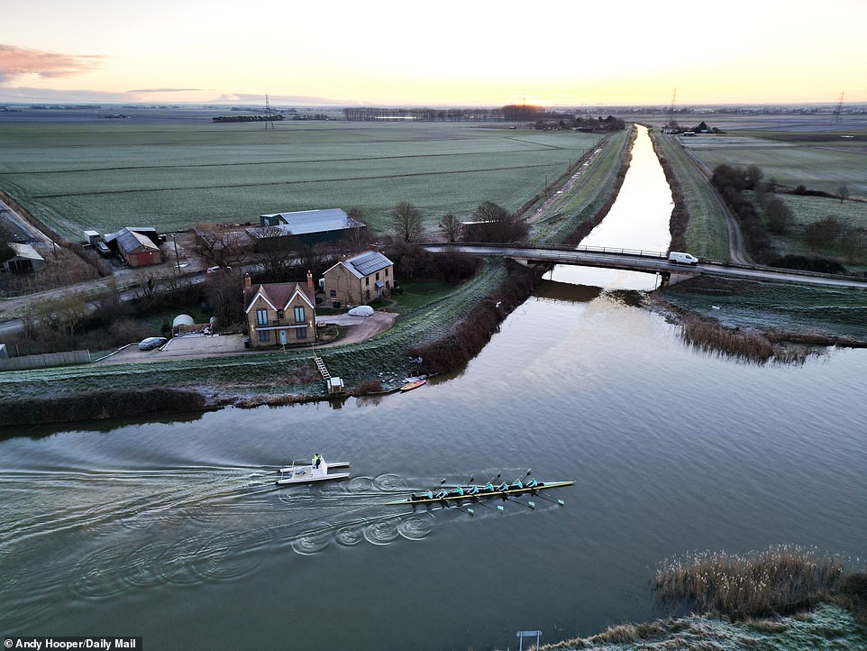 The Cambridge team rows past acres of fields, a small bridge and a small group of riverside houses