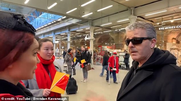The tourists, wearing red scarves, gathered around the pianist, who repeatedly explained to them that he was allowed to film because they were in a public place.  “We are in Britain, we are not in China,” he added