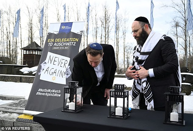 During his visit, Musk lights a candle behind a sign that echoes the slogan: Never again