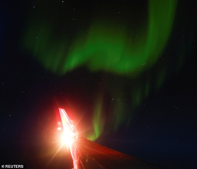 An aurora is caused by disturbances in the Earth's magnetosphere due to a stream of particles from the Sun and is usually located around the Earth's magnetic poles.  It is pictured here through the window of an airplane flying between Spitsbergen and Tromsø, Norway on January 5, 2024