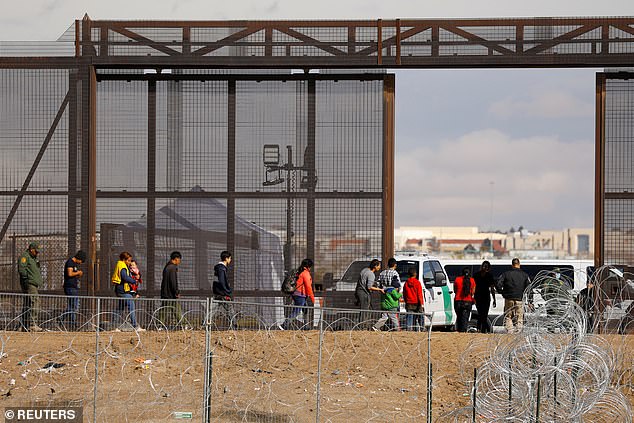 Asylum seekers walk past the fence at the U.S.-Mexico border as they wait to be processed in El Paso
