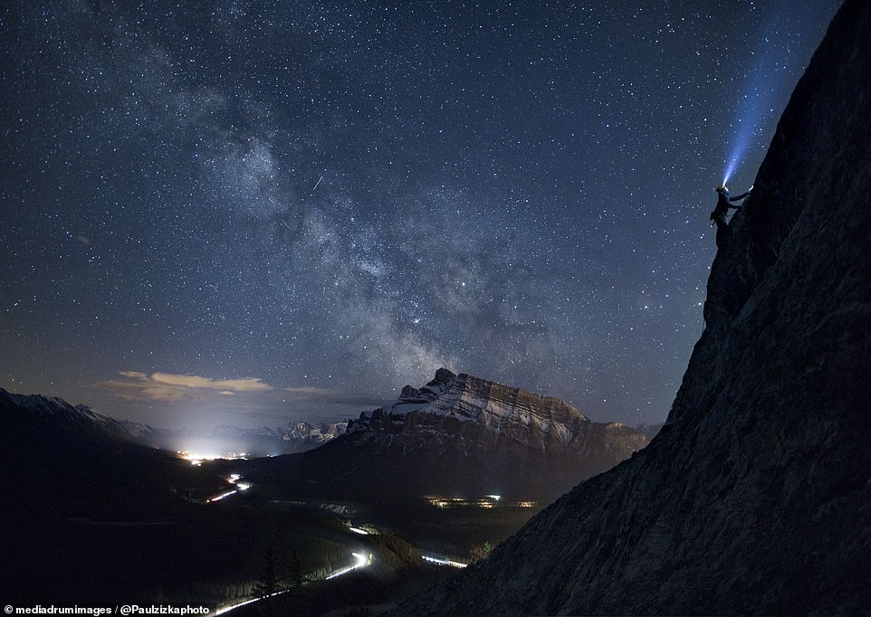 Also taken in Banff, this shot shows a mountain climber wearing a headlamp as lights shine from a road and houses below