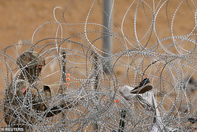 A Border Patrol agent inspects a shoe hanging in barbed wire set up to impede the crossing of migrants into the US