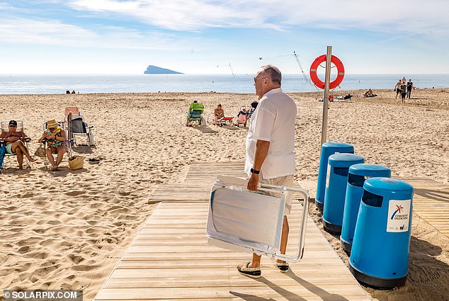 A man looks for a spot on the beach in Benidorm, Spain, with a lounger