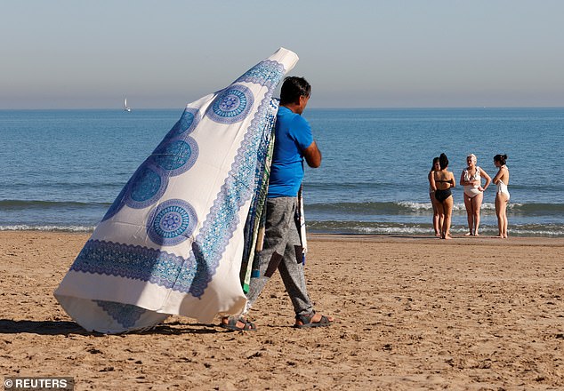 A towel seller walks along the beach of Mavarrosa in Valencia, Spain on Thursday