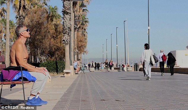 A topless man soaks up the sun on a promenade in Spain during sweltering temperatures