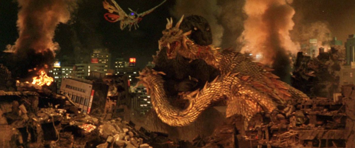 Godzilla bites King Ghidorah's neck with a destroyed city in the background and Mothra flies towards them.