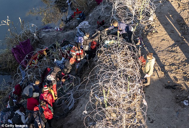 Migrants are seen pushing their way through barbed wire in Eagle Pass in December 2023.  The Texas city is one of three cities that will host the latest convoy later this month.