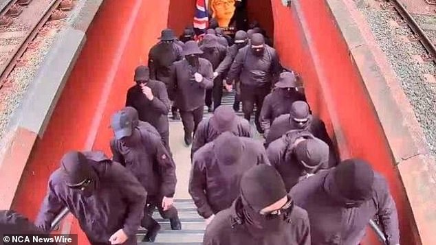 You see the group of men boarding a train in all black, one of which is carrying an Australian flag