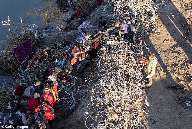 As seen from an aerial photo, immigrants climb through barbed wire after crossing the Rio Grande from Mexico in Eagle Pass, Texas, on December 18