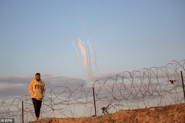 Rockets are fired from the Gaza Strip (background) as a displaced Palestinian walks along the Palestinian-Egyptian border in the Rafah camp, January 29