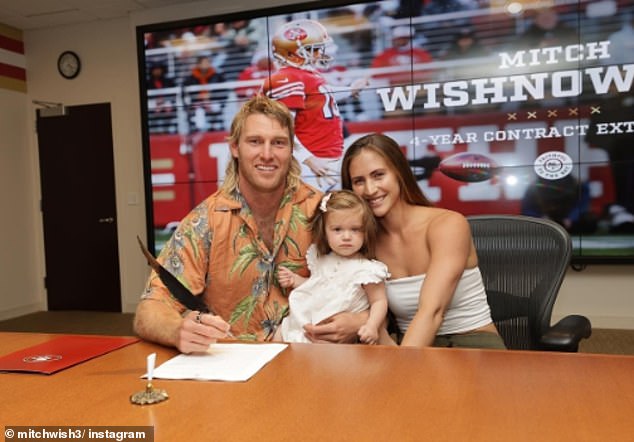 Wishnowsky, wife Maddie and their daughter Bowie are pictured signing the contract that made his long struggle to break into the gridiron more than worth it