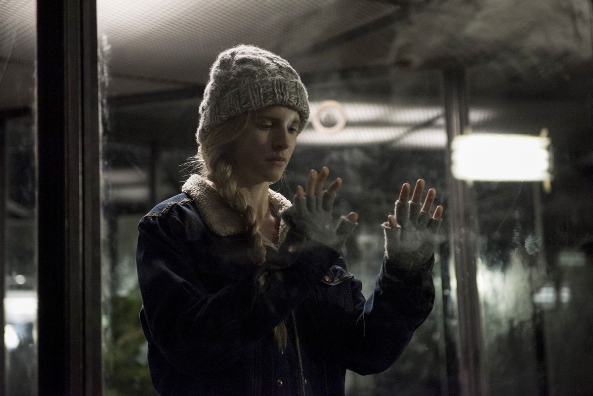 Prairie Johnson in a coat, knit hat and fingerless gloves presses her hands against a smudged window in The OA.